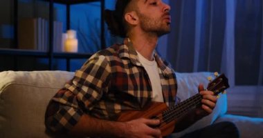 Genç adam evde gitar çalıp şarkı söylüyor.