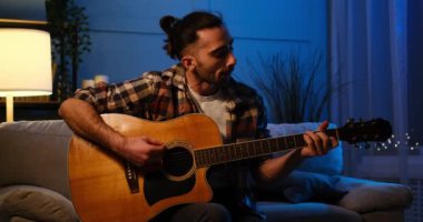 Evde gitar çalan ve şarkı söyleyen bir adam
