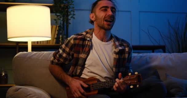Man singing and playing ukulele guitar at home — Stock Video