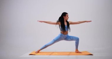 Virabhadrasana savaşçısı pozu veren genç bir kadın.