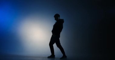 Genç adam mavi ışıkta hiphop tarzında dans ediyor.