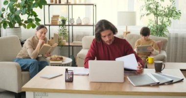 Annesi kitap ve oğlu dijital tablet kullanarak belgeleri analiz eden bir adam.