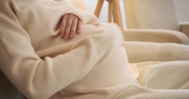 Hamile bir kadın evde karnını okşuyor.