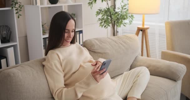 Zwangere vrouw met behulp van mobiele telefoon thuis — Stockvideo