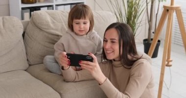 Annesiyle evde cep telefonu izleyen bir kız.