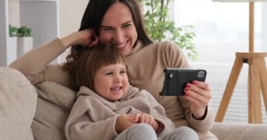 Annesiyle evde cep telefonu izleyen bir kız.