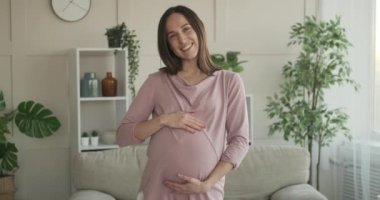 Hamile bir kadın evde karnını okşuyor.