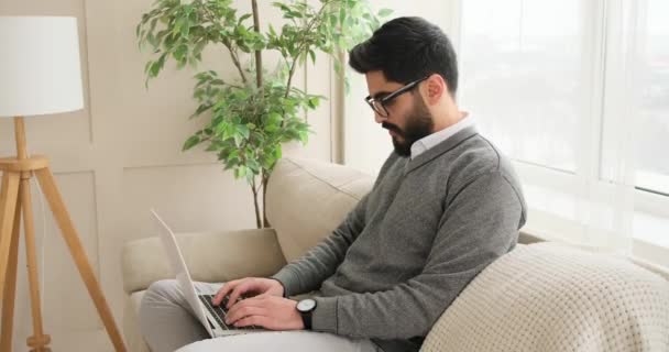 Hombre usando el ordenador portátil en el sofá en casa — Vídeo de stock