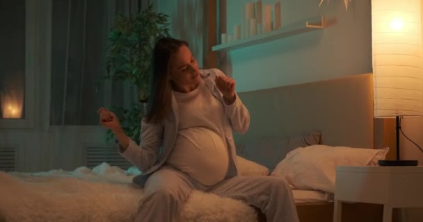 밤에 침대에 앉아 춤을 추는 임신부 — 비디오
