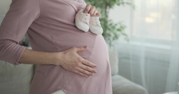 Kvinna som håller babyskor på sin gravida mage hemma — Stockvideo