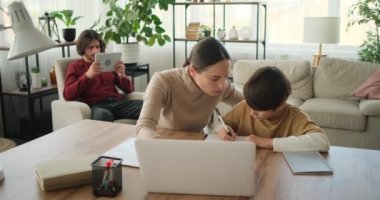 Oğlu ve annesi ödev yaparken dizüstü bilgisayar ve babası dijital tablet kullanıyor.