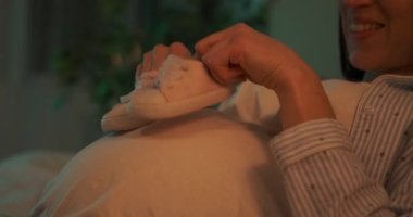 Hamile karnında bebek ayakkabıları taşıyan mutlu bir kadın.