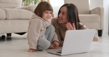 Anne ve kızı evde dizüstü bilgisayar izlerken el sallıyorlar.