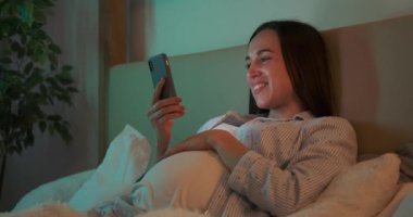 Hamile kadın evde cep telefonu kullanıyor.