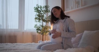 Hamile kadın yatakta karnını okşuyor.