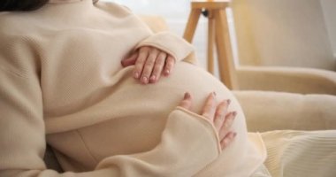 Hamile bir kadın evde karnını okşuyor.