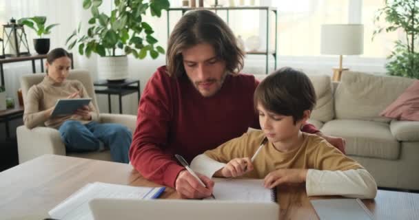 Hijo con padre haciendo deberes y madre usando tableta digital — Vídeos de Stock