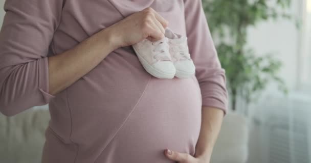 Kvinna som håller babyskor på sin gravida mage hemma — Stockvideo