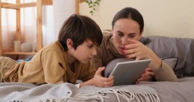 Anne ve oğlu yatakta dijital tablet kullanıyor.