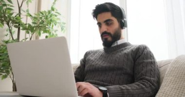 Adam kulaklıkla müzik dinliyor ve dizüstü bilgisayarla çalışıyor.