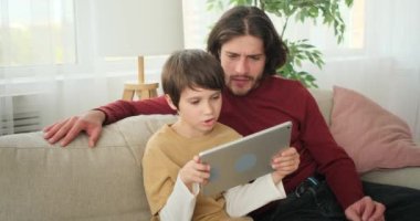 Baba oğlunun dijital tabletle oynamasını izliyor.