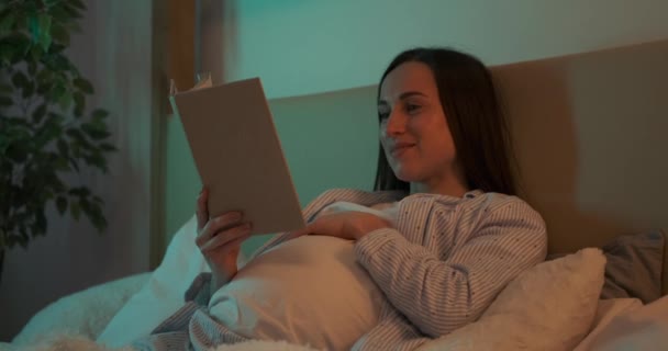 Pregnant woman reading book on bed at home — Stock Video