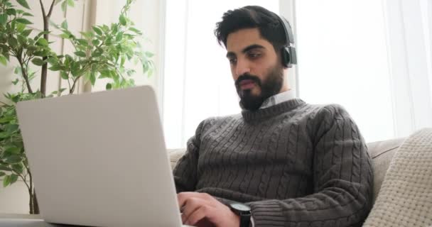 Hombre disfrutando de la música en los auriculares y trabajando en el ordenador portátil — Vídeos de Stock