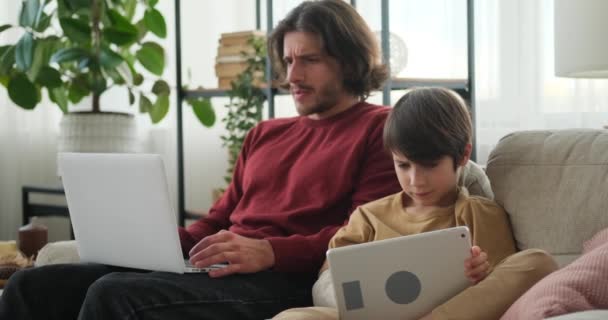 Hombre escribiendo en el ordenador portátil y el hijo utilizando la tableta digital — Vídeo de stock