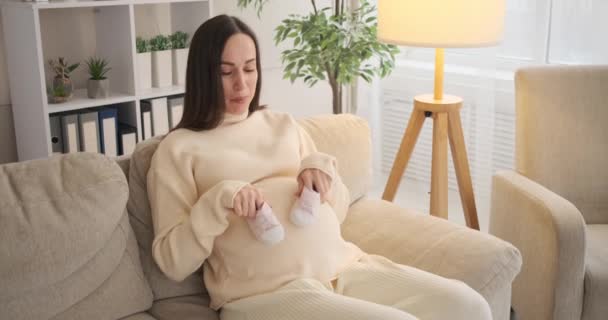 Gelukkig vrouw wandelen baby shoes op haar zwanger buik thuis — Stockvideo
