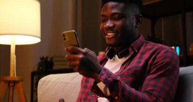 Afrikalı Amerikalı erkek cep telefonu kullanarak ve kahve içerek mesaj atıyor.