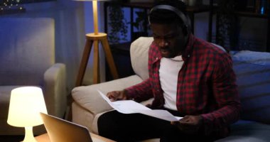 Adam bilgisayarla çalışıyor ve kulaklıkla müzik dinlerken belgeleri analiz ediyor.