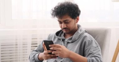 Genç adam koltukta cep telefonu kullanıyor.