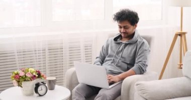 Dizüstü bilgisayar kullanan genç adam koltukta oturuyor.