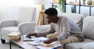 Genç adam dizüstü bilgisayar kullanıyor ve evrak işlerini yapıyor.