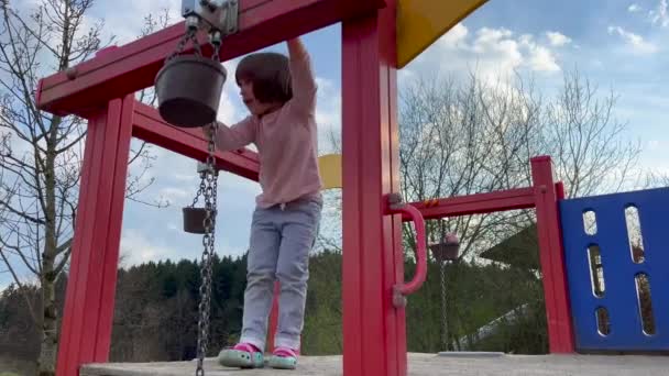 Girl standing on bridge with bucket hanging on chain — Vídeo de stock