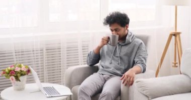 Genç adam kahve içerken dizüstü bilgisayar kullanarak sohbet ediyor.