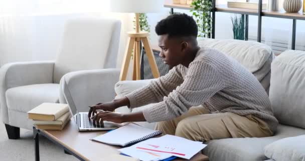 Афроамериканец использует ноутбук и делает бумажную работу — стоковое видео