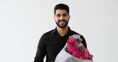 Genç adam gülümsüyor ve elinde çiçek buketi tutuyor.