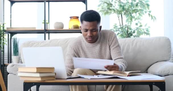 Afrikai amerikai férfi laptopot használ és papírra ír — Stock videók