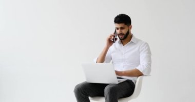 Dizüstü bilgisayar kullanırken cep telefonda konuşan adam