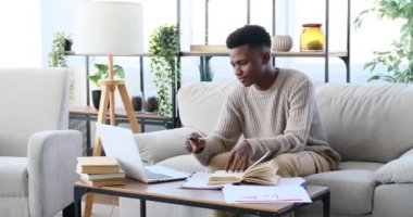 Genç adam dizüstü bilgisayar kullanıyor ve kağıda yazıyor.