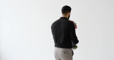 Mutlu genç adam dönüyor ve beyaz arka planda çiçek buketi veriyor.