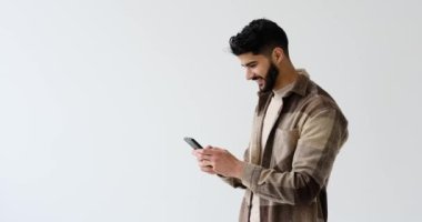 Mutlu genç adam beyaz arka plan üzerinden cep telefonuna mesaj atıyor.