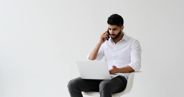 Snygg Man Diskuterar Mobilsamtal När Använder Laptop Mot Vit Bakgrund — Stockvideo