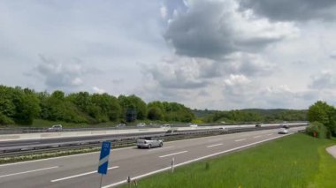 Cars speeding on highway road by rural landscape against cloudy sky