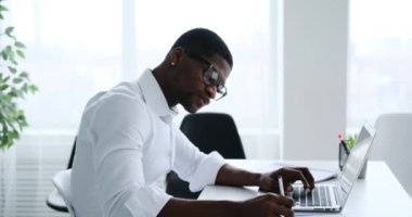 Afrikalı Amerikalı iş adamı laptopta çalışıyor ve ofiste notlar yazıyor.