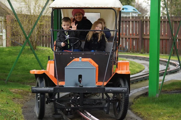 Família jovem em um carro laranja passeio de fairgound — Fotografia de Stock