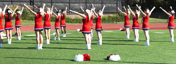 Rear view of high school cheerleaders practicing their routine before they put on their half time show.