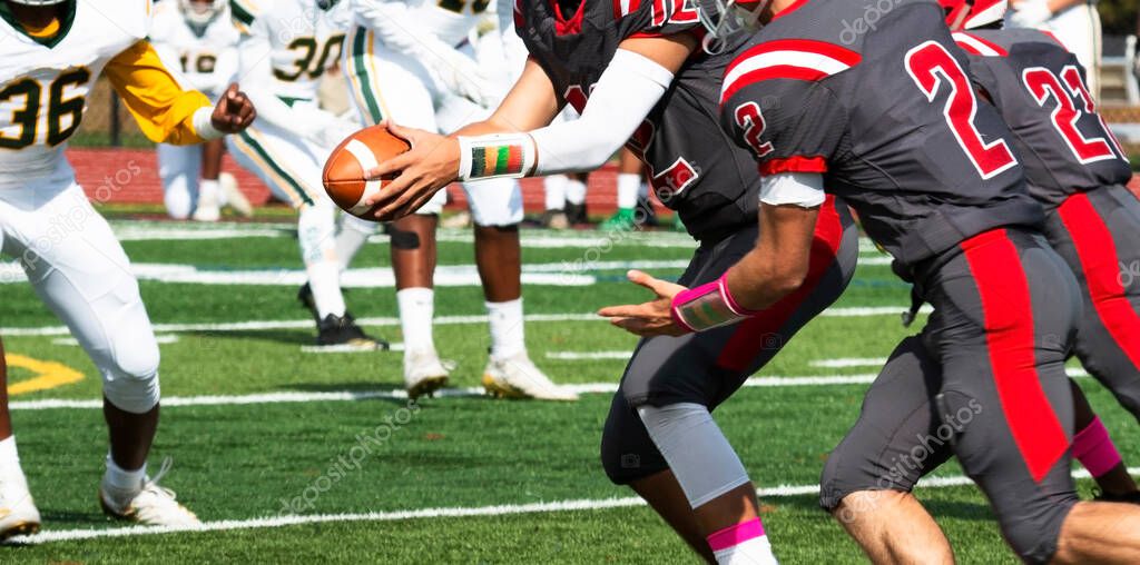 Football quarterback handing off the ball to his running back during a high school game.