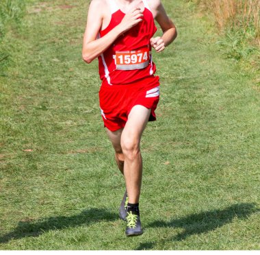 Yokuş aşağı bir çim tarlasında 5K koşan liseli bir çocuğun ön görüntüsü..